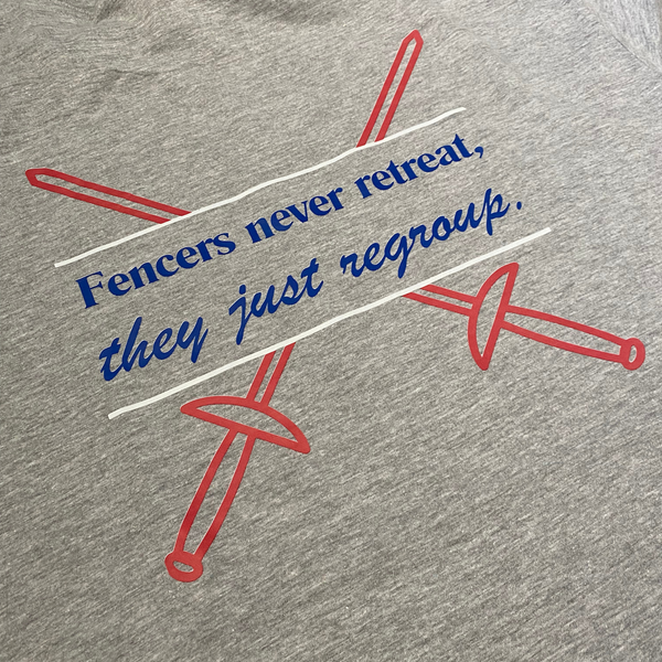 A closeup of the blue words, "Fencers never retreat, they just regroup." are bordered by bright white lines, and two crisp, red sword outlines, crisscross behind, adding a patriotic touch. Adult heathered grey shirt.