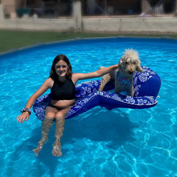 Close up picture of retro flower power swim scrunchie on wrist pictured with matching swim scARF (aka cooling bandana for dogs) on a cream goldendoodle. They are sitting on a raft in a pool together. Pipevine Designs.