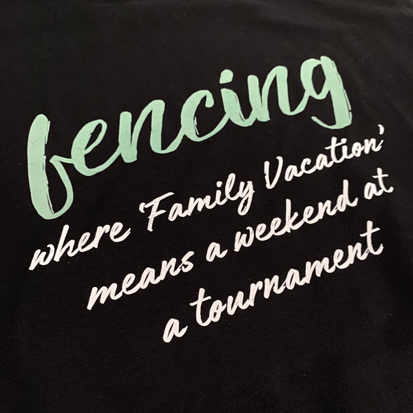 closeup of the cursive word "Fencing" in a mint green color, floating above the humorous white sentence, "Where family vacation means a weekend at a tournament". Adult black shirt.