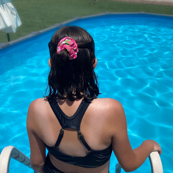 Close up picture of floral print with lime green on hot pink swim scrunchie in hair, by a pool. Pipevine Designs.